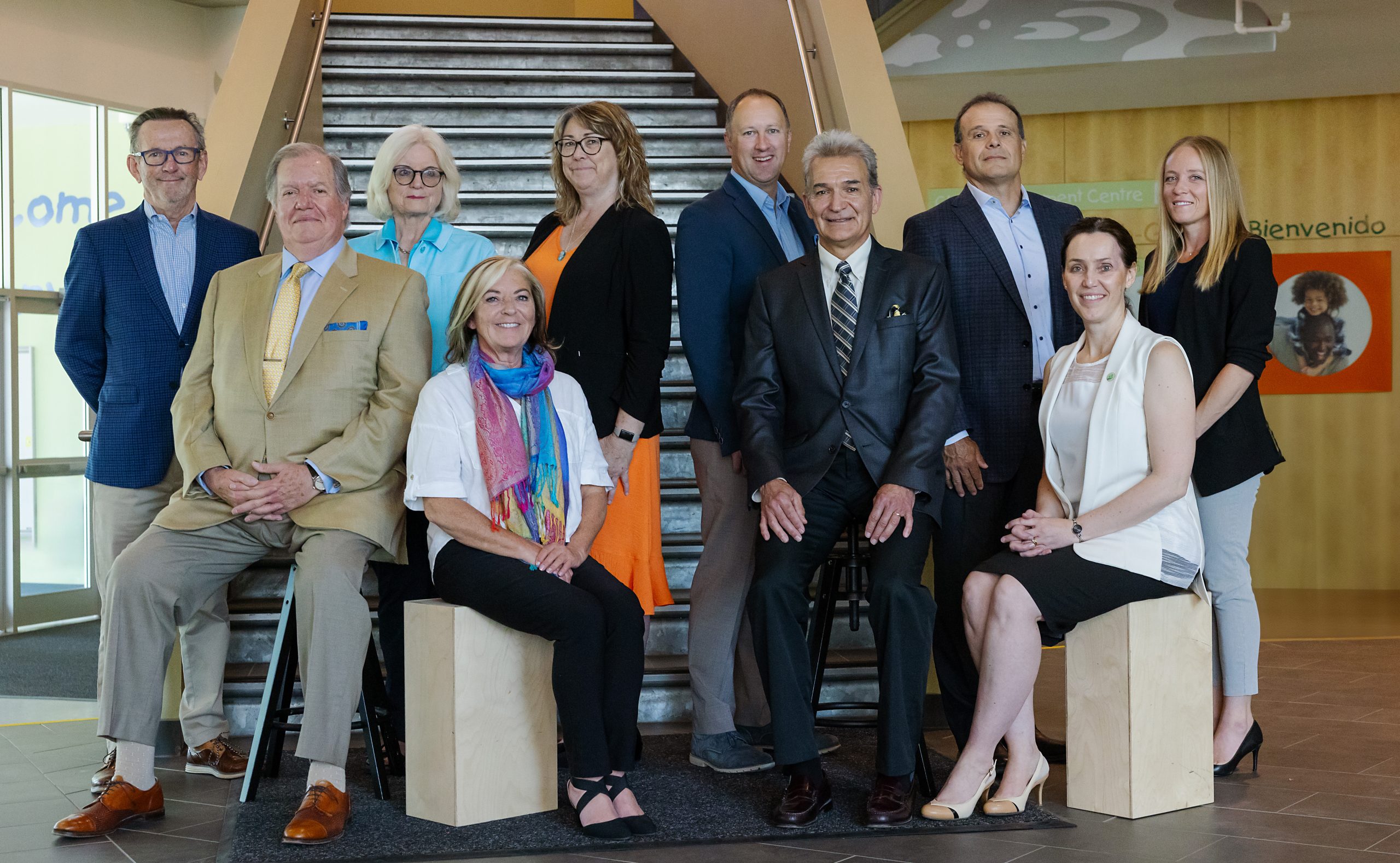 Group portrait of eleven individuals in business or semi-casual attire, posed in two rows in front of a set of metal stairs. The individuals are the Board of Directors of The Sinneave Family Foundation.