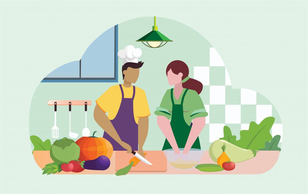Two people are in a kitchen, working side by side at a cutting board. One is wearing a chef's hat and holding a knife, there are various fruits and vegetables on the counter.